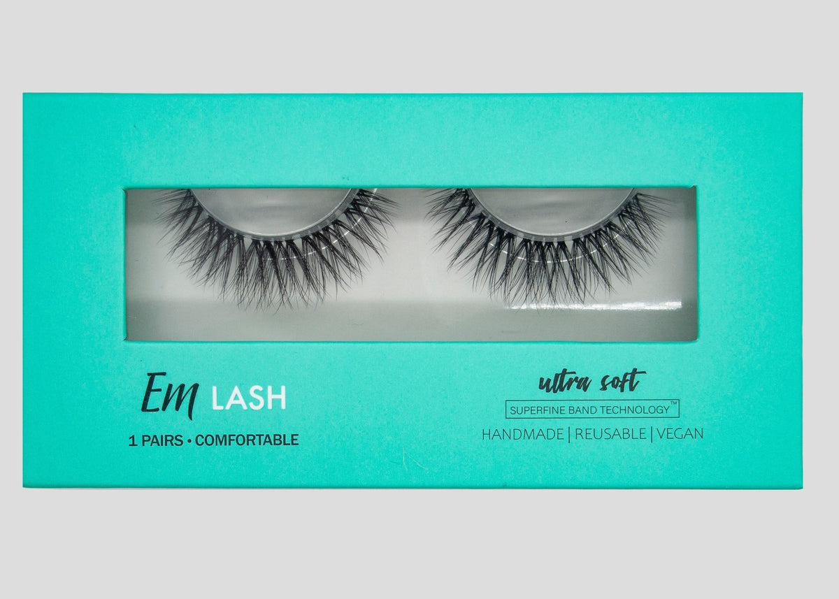 Em Lash false eyelashes in a bright turquoise box with a clear window showing the two pairs of lashes inside. The packaging also features white text reading 'Em LASH', 'ultra soft', and 'HANDMADE | REUSABLE | VEGAN'.