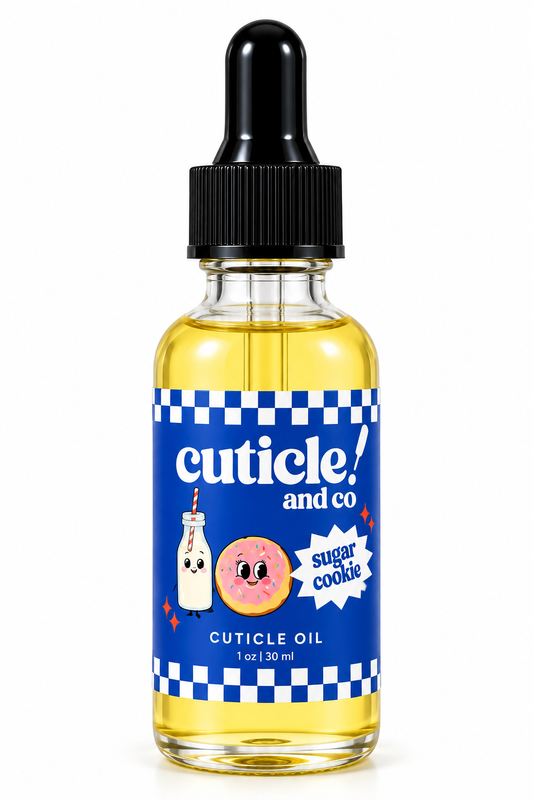 A 1 oz bottle of Cuticle Oil by Cuticle! and Co. The clear glass bottle shows the yellow oil inside, topped with a black dropper cap and wrapped in a blue label with a checkered border and cartoon donut and milk bottle illustrations.